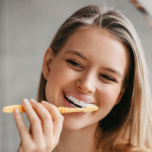 Woman brushing teeth with yellow toothbrush.