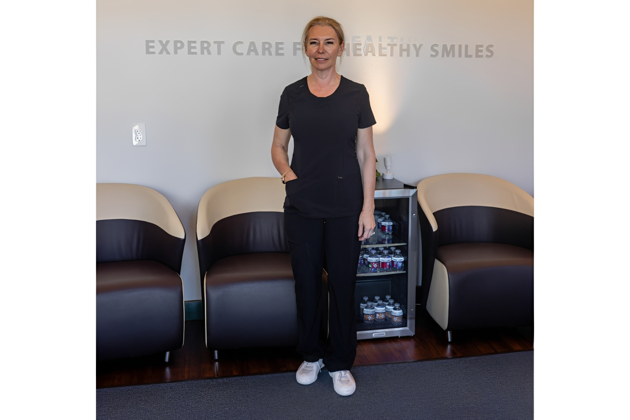 A smiling dental professional stands in a modern clinic waiting area.